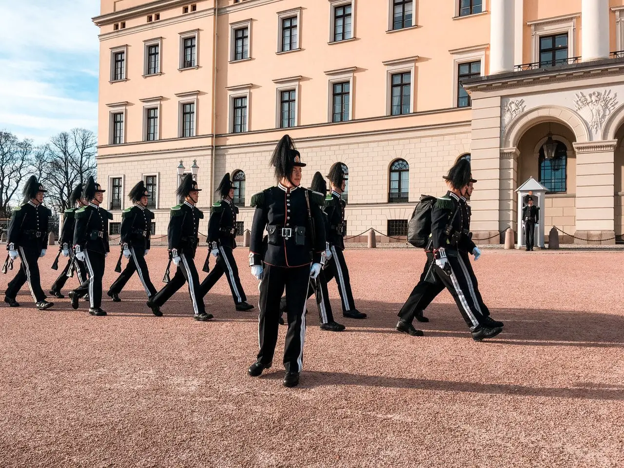 Changing of the guards ceremony at Oslo Royal Palace, Norway, featuring numerous guards in black uniforms marching in front of the Oslo Royal Palace