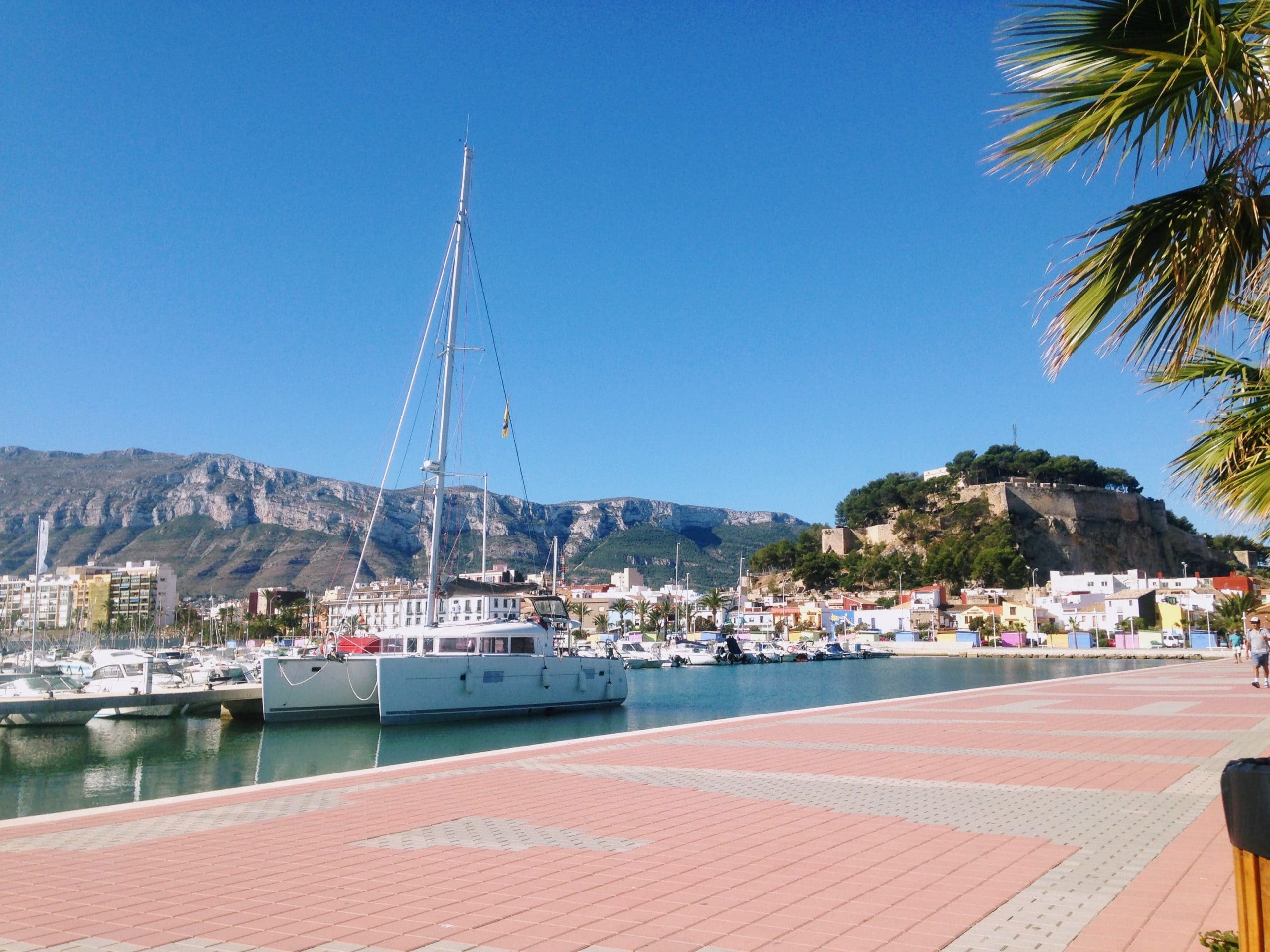 Denia port and harbour in spain with the Denia castle in the background. You can see a small boat in the water.