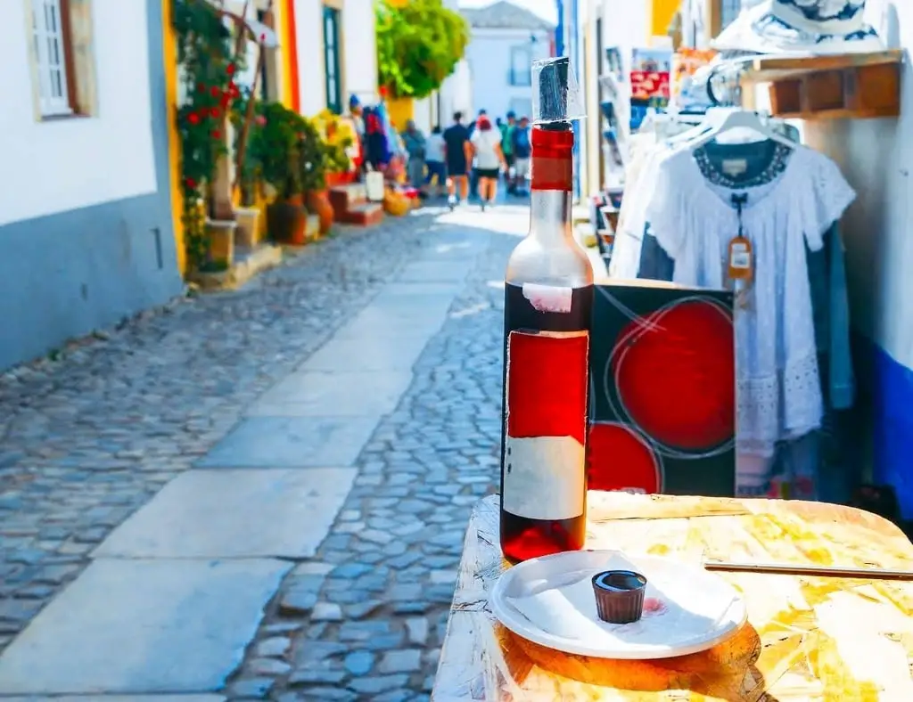 A bottle of Ginja de Obidos on a table, with a chocolate ginja cup in front of it.