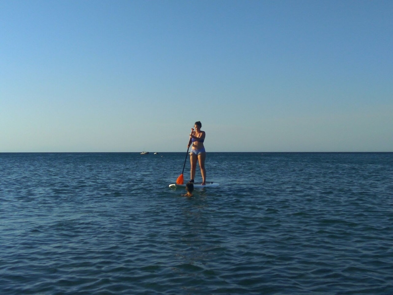 Ella stand up paddleboarding on the ocean in summer.