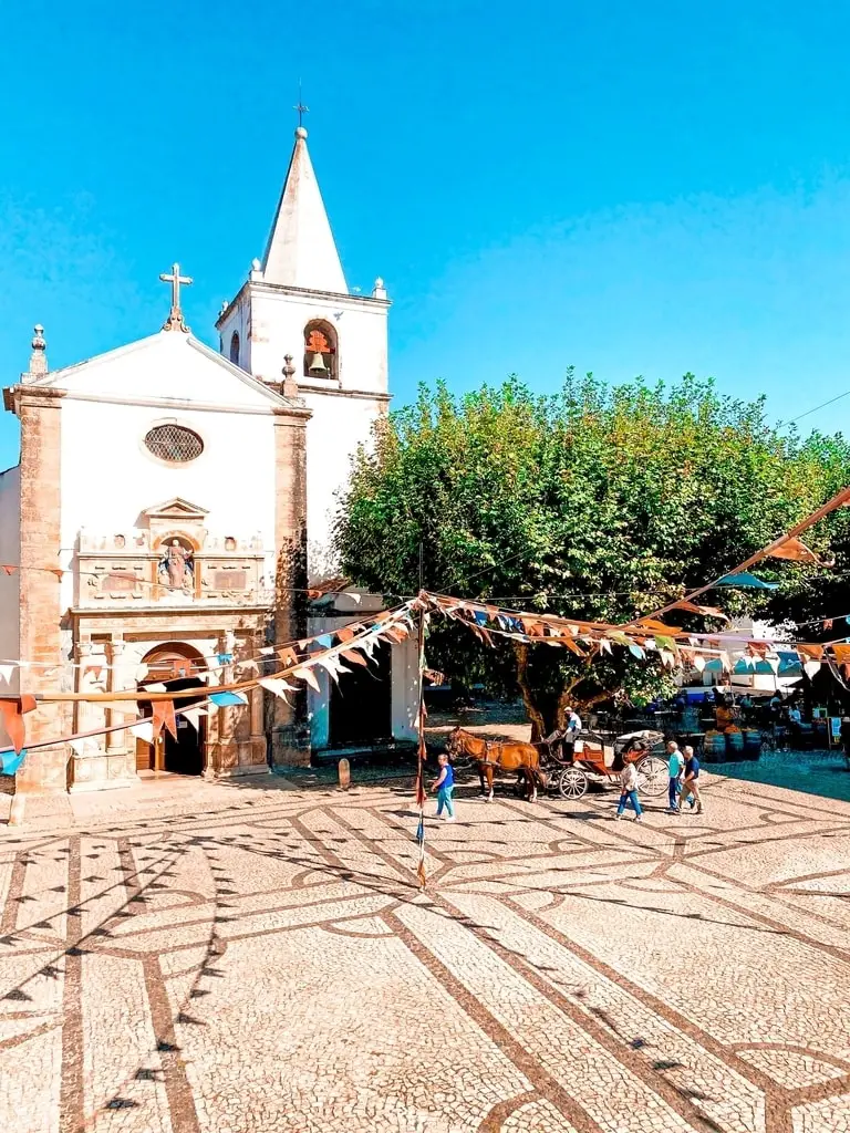 Santa Maria church in Óbidos, Portugal. In front of the church is colourful bunting and a man riding a horse and cart.