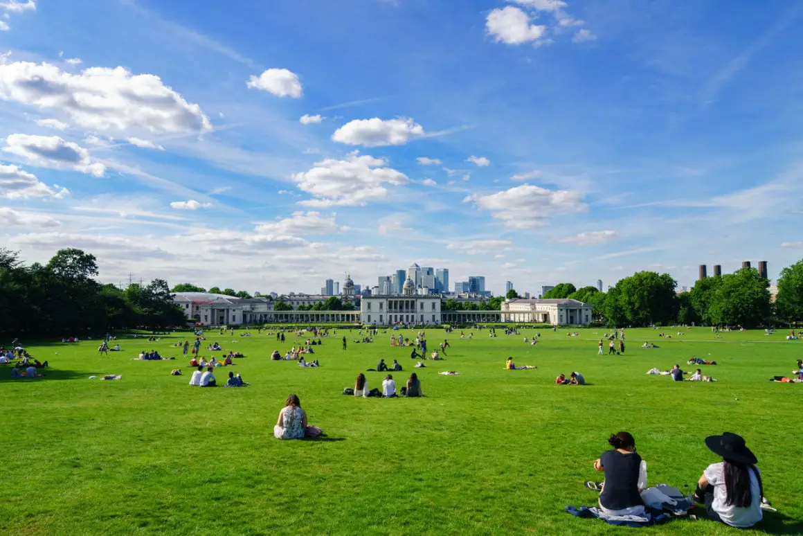 People sitting on the grass in Greenwich Park, with the London skyline in the background.