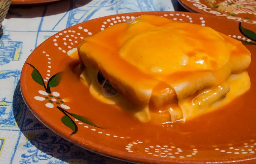 Francesinha sandwich, a sandwich topped with a fried egg and cheese and doused in a rich gravy-like beer sauce. This is a traditional dish unique to Porto.