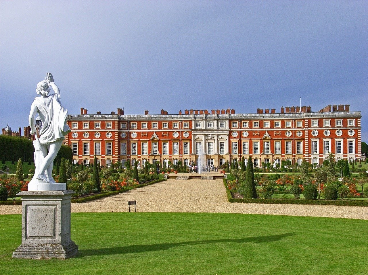 Red and white palace in London with well-manicured lawns and gardens in front of it.