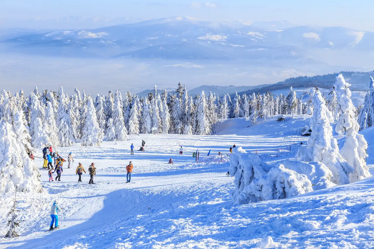 People skiing and snowboarding in Szczyrk, Poland, with a winter view of Skrzyczne peak in the Beskid Mountains in the background.