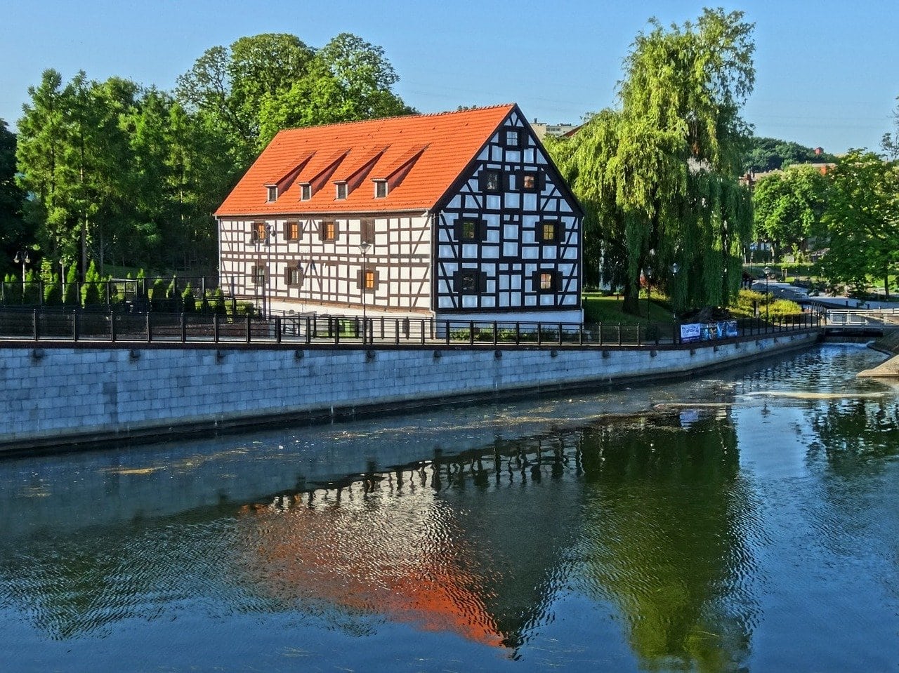 A serene view of a traditional half-timbered house by a calm river in Bydgoszcz, captured on a day trip from Poznan, Poland. 