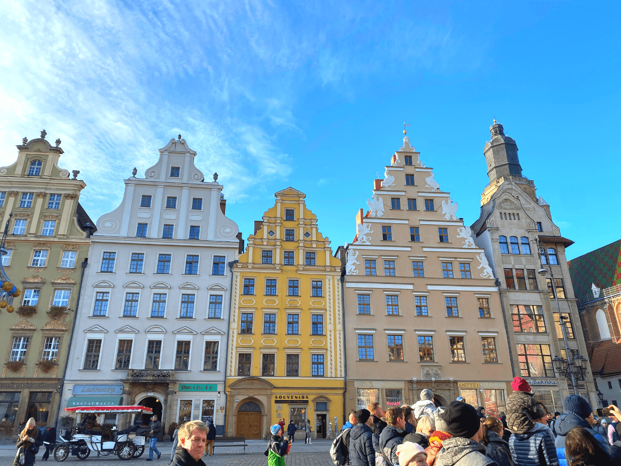 Visitors gather in a bustling market square in Wroclaw, admiring the distinctive historical buildings with ornate facades, ideal for a cultural day trip from Poznan.