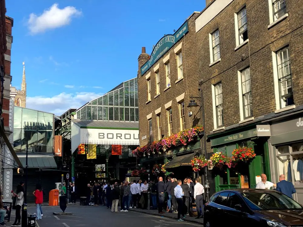 Borough Market, in the London Borough of Southwark, on a sunny say. The Market Porter pub is on the right side, in front of the market.