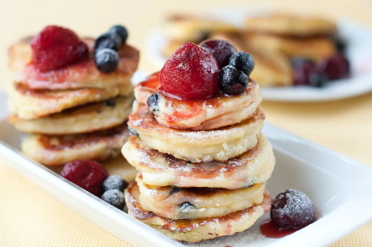 Two stacks of mini pancakes, topped with blueberries, raspberries and syrup.