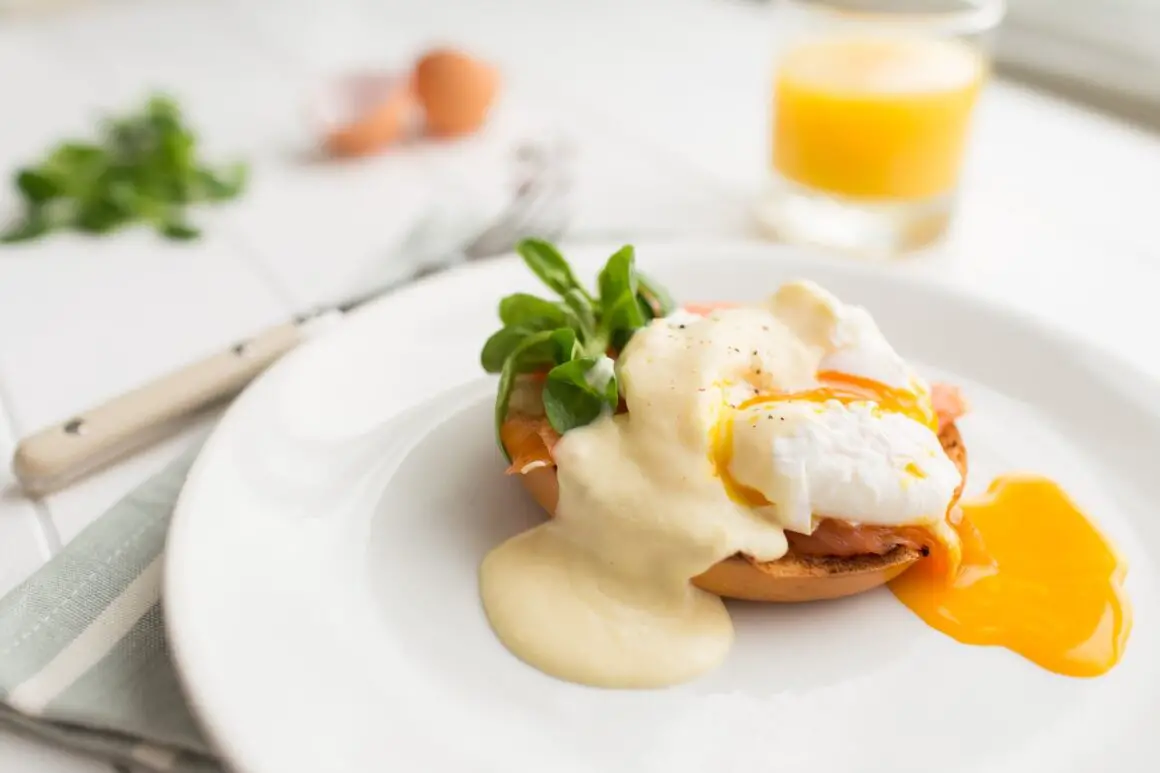 Eggs benedict with runny yolk and hollandaise sauce on a white plate.