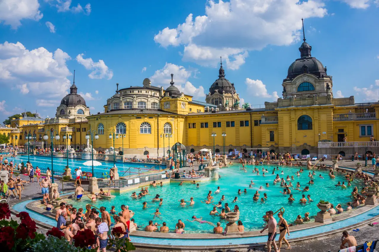 Yellow buildings of Széchenyi Thermal Baths, with a large outdoor pool filled with bathers in front. This is a must-visit when spending 48 hours in Budapest.