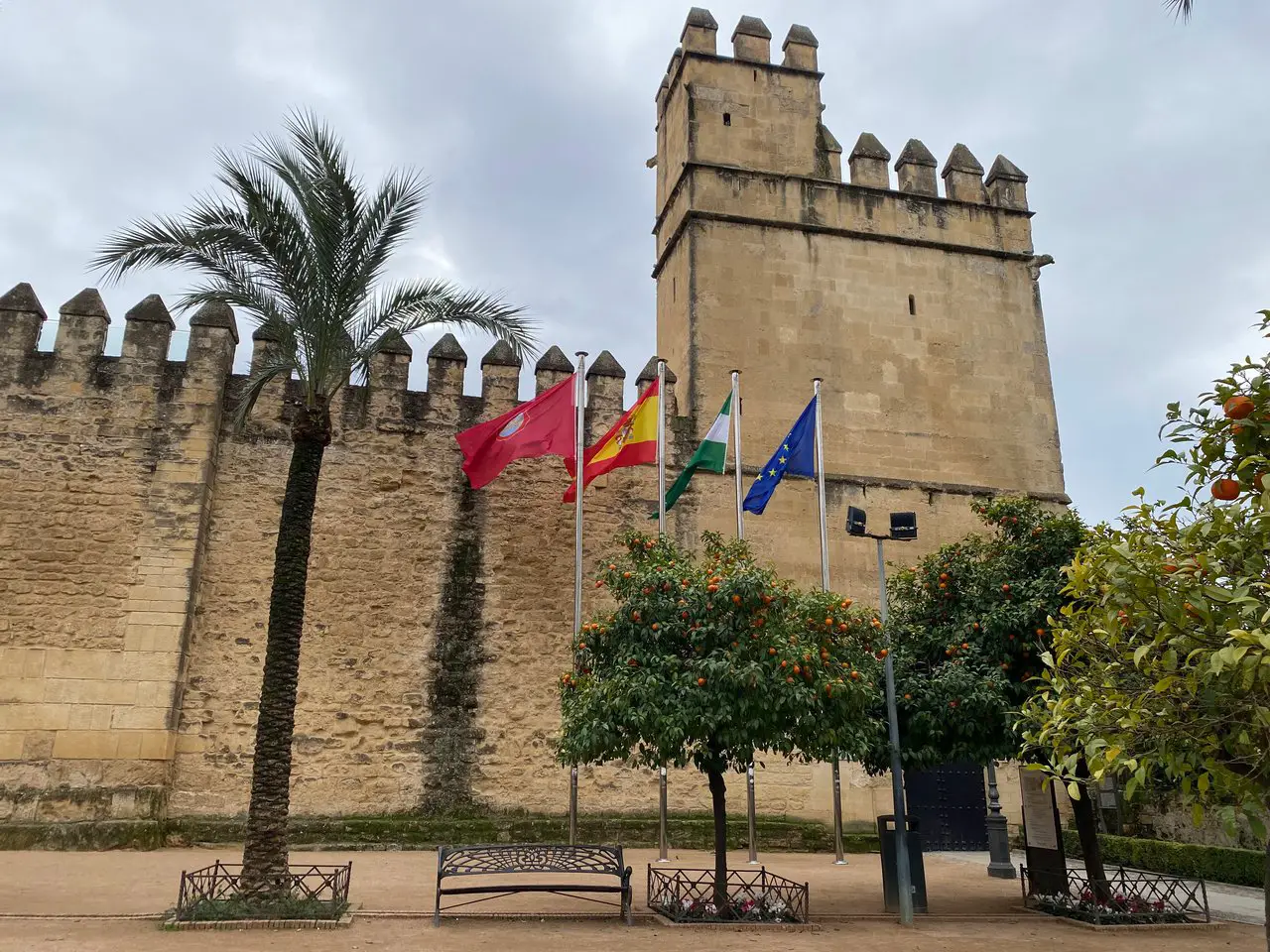 Exterior of the Alcazar of the Christian Monarchs. A tall castle tower stands behind numerous flags fluttering in the wind.