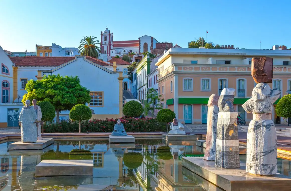 The main plaza in Silves, Portugal, containing fountains, statues, and pastel-coloured buildings