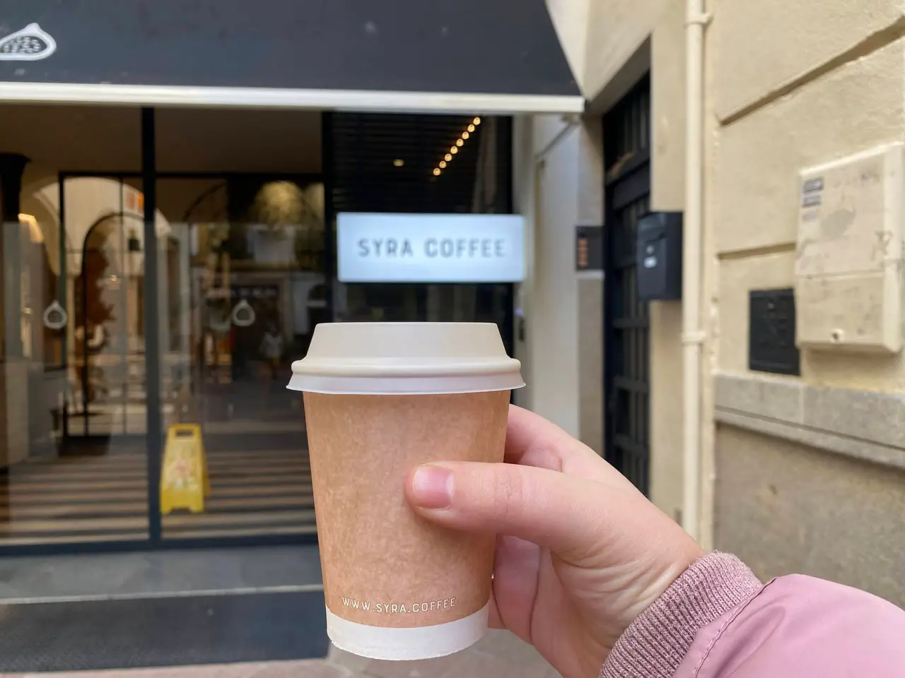A coffee cup is held in front of the Syra coffee shop.