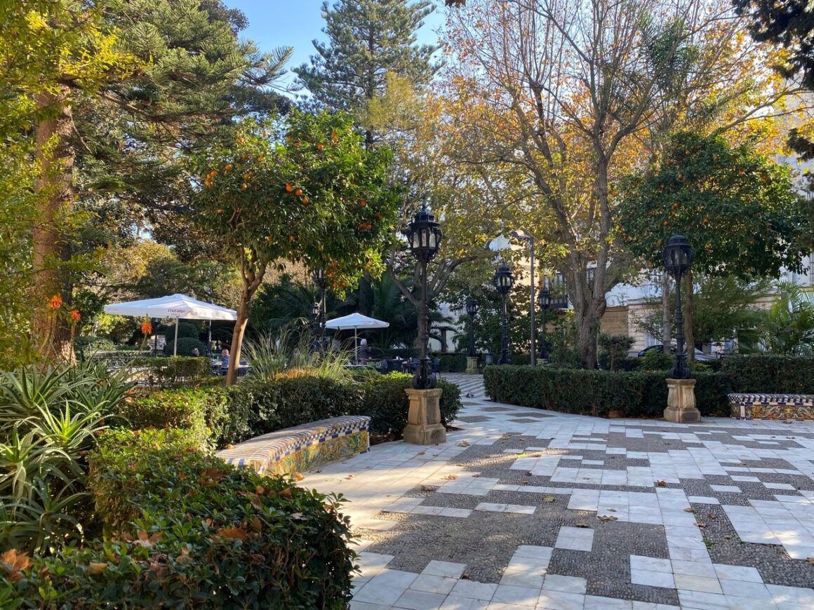 Green park shaded by trees with a cobbled plaza in the middle