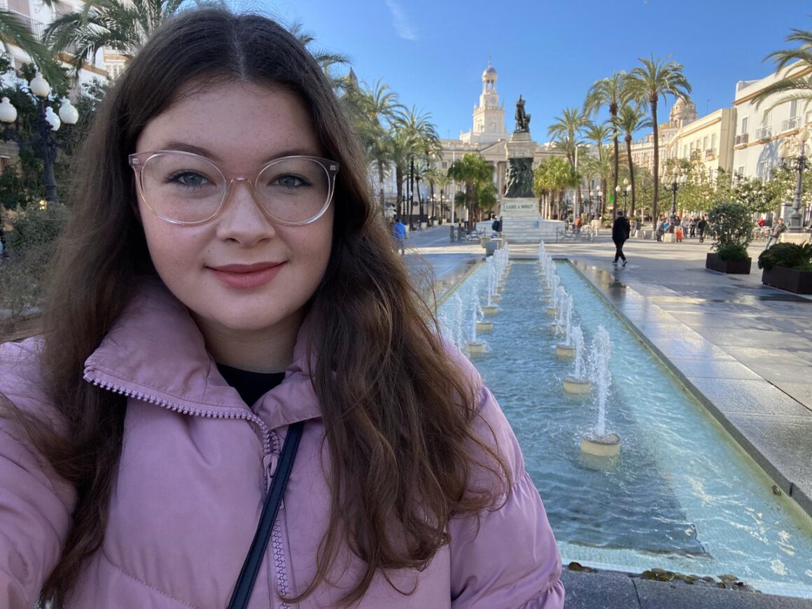 Ella smiling on a day trip to Cadiz, standing in front of fountains and a statue.