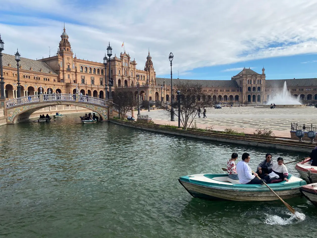 Plaza de Espana in Seville Spain. A bridge is standing over a small moat, and a man is rowing a boat in the moat.