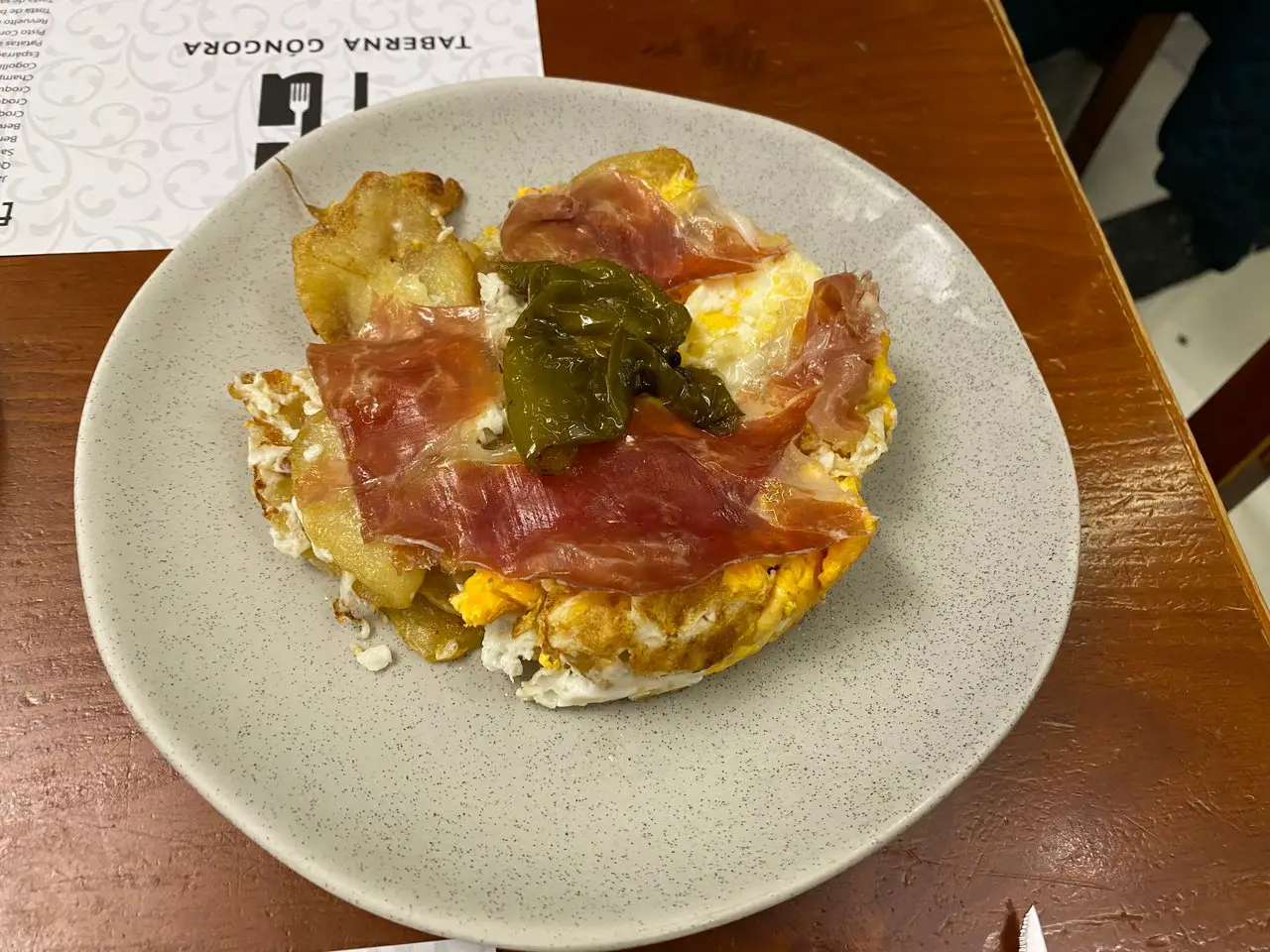 A potato, egg and cured ham dish on a plate.