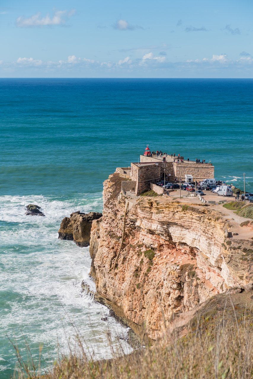 Nazare's red lighthouse on cliffs, with the ocean below. This is the Nazare big wave view point