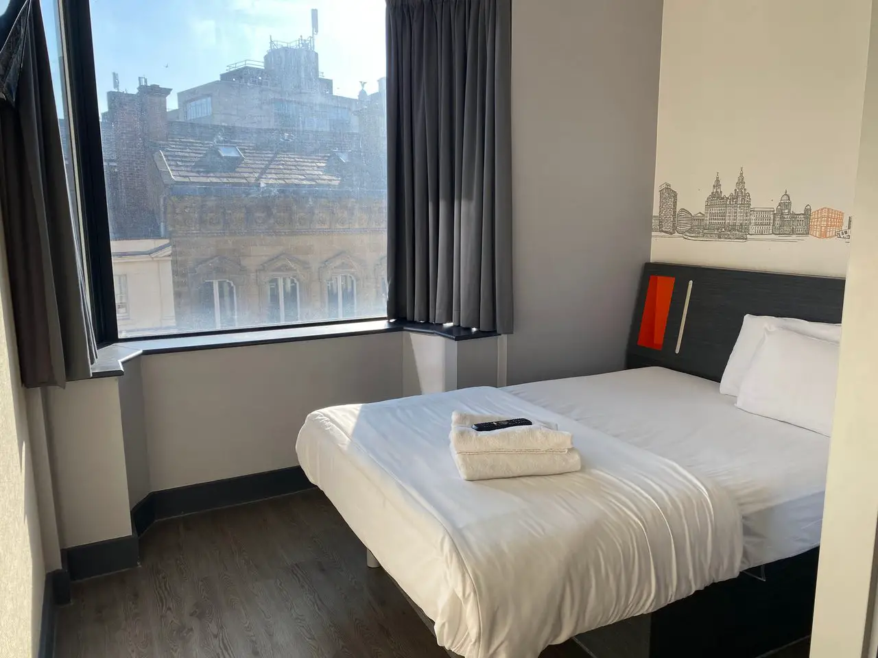 Inside a bedroom at the EasyHotel in Liverpool, showing a double bed with white sheets and a window looking out to Georgian buildings