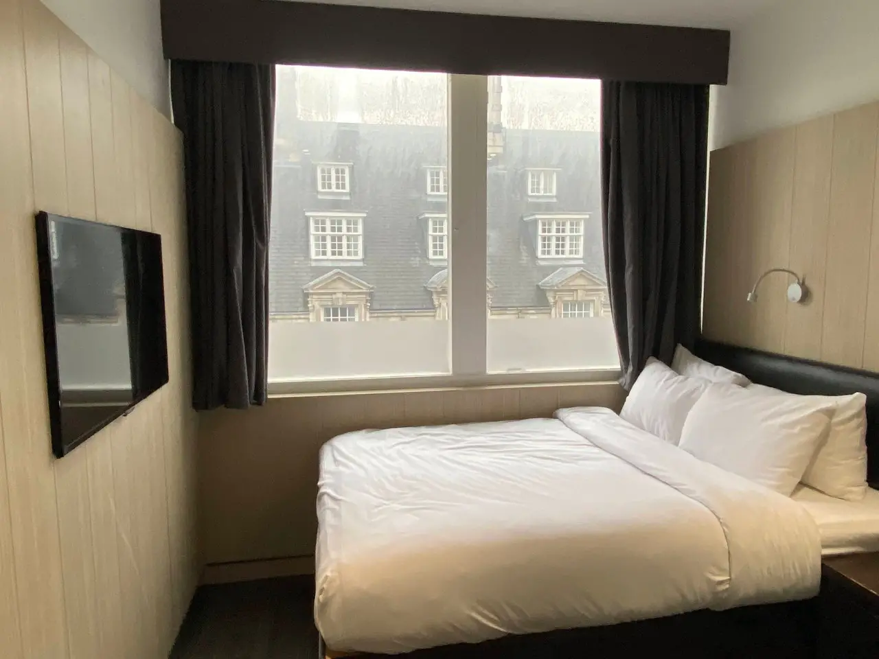 Inside a bedroom at the Z Hotel in Liverpool, showing a double bed with white sheets, brown curtains, and a flat-screen TV on the wall.