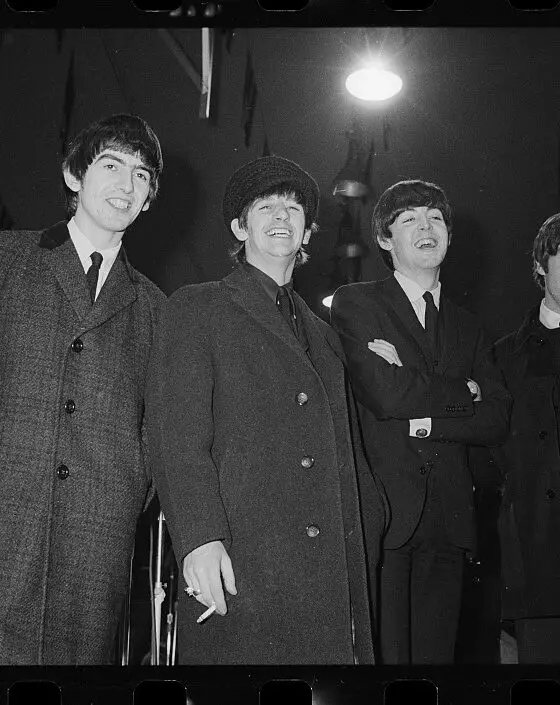 Black and white image of the four members of the beatles wearing large overcoats.