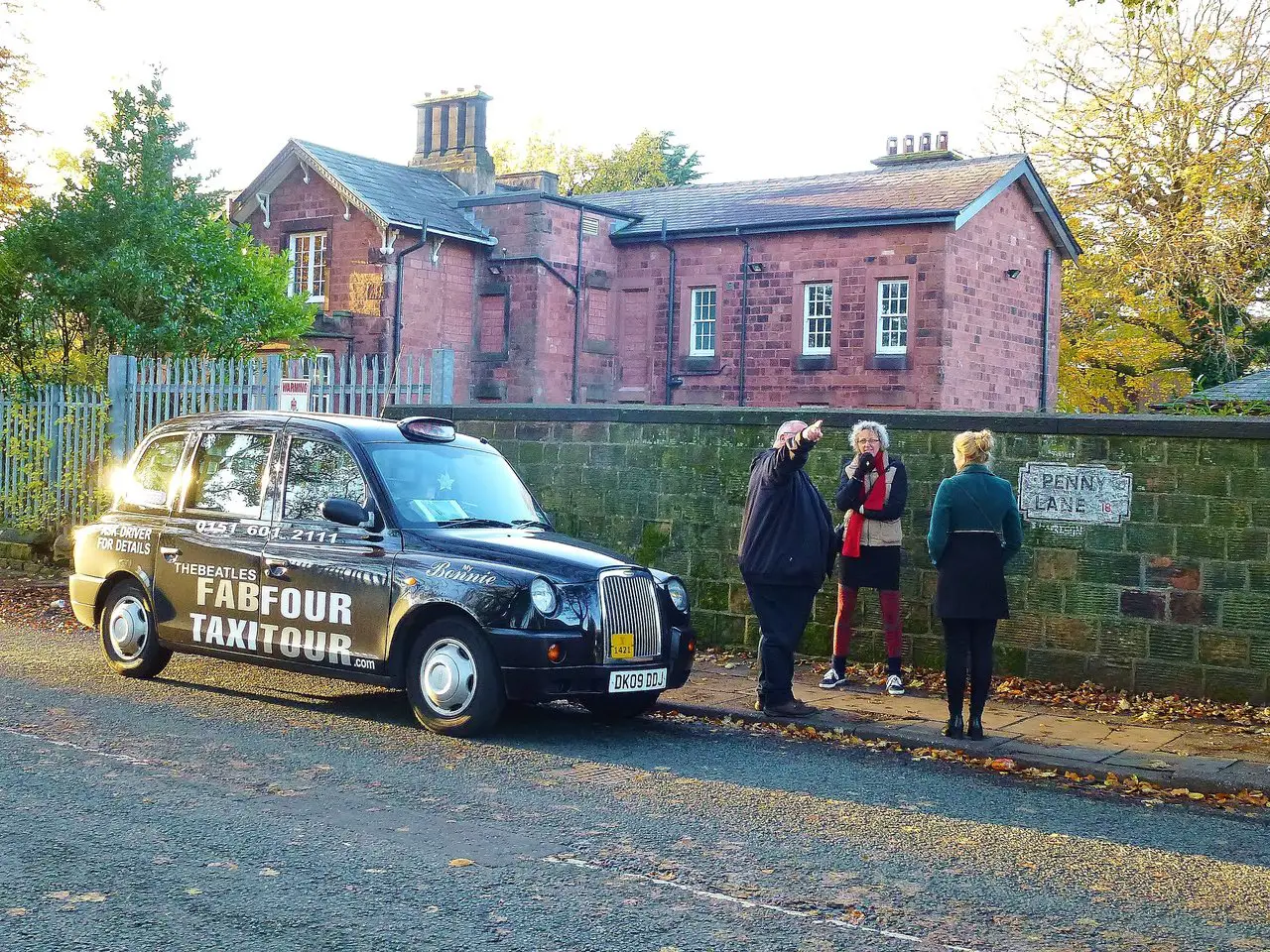 Liverpool Fab Four Taxi Tours - a black cab parked on Penny Lane as a guide points out the sights to two female tourists.