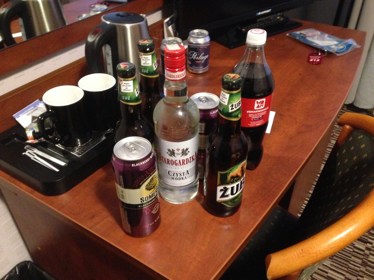 A collection of Polish alcoholic beverages including Zubrówka Bison Grass Vodka and Tyskie beer, arranged on a cluttered tabletop in a hotel room. In Poland, the legal drinking age is 18.