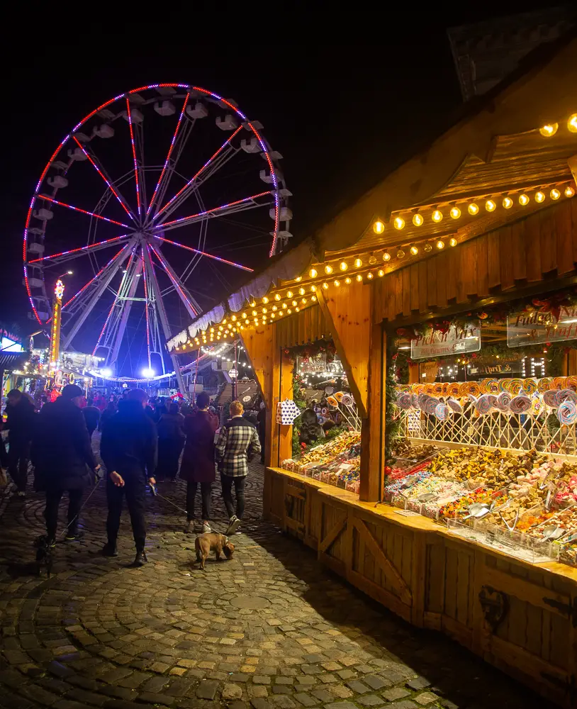 A wooden hut selling trinkets at night at Liverpool Christmas Market with a ferris wheel in the background