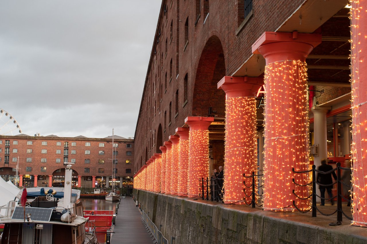 The red pillars of the Albert Dock in Liverpool covered in red Christmas lights at dusk