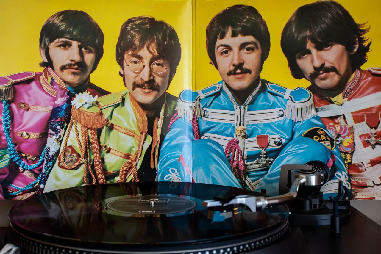 The four Beatles dressed in their psychedelic Sgt Peppers costumes, with a vinyl playing in the foreground.
