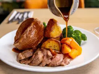 A Sunday roast in Liverpool - roast beef, roast potatoes, yorkshire pudding and broccoli on a white plate with gravy being poured over it