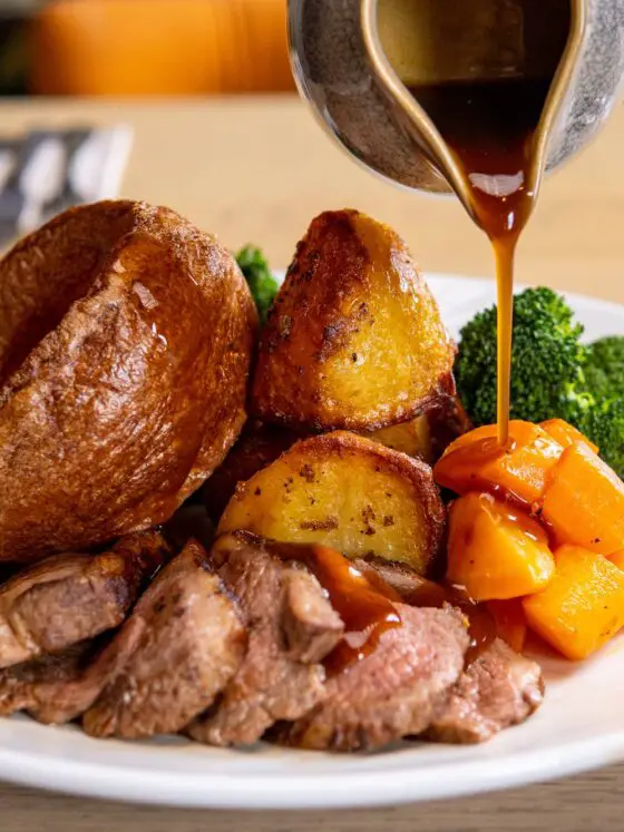 A Sunday roast in Liverpool - roast beef, roast potatoes, yorkshire pudding and broccoli on a white plate with gravy being poured over it