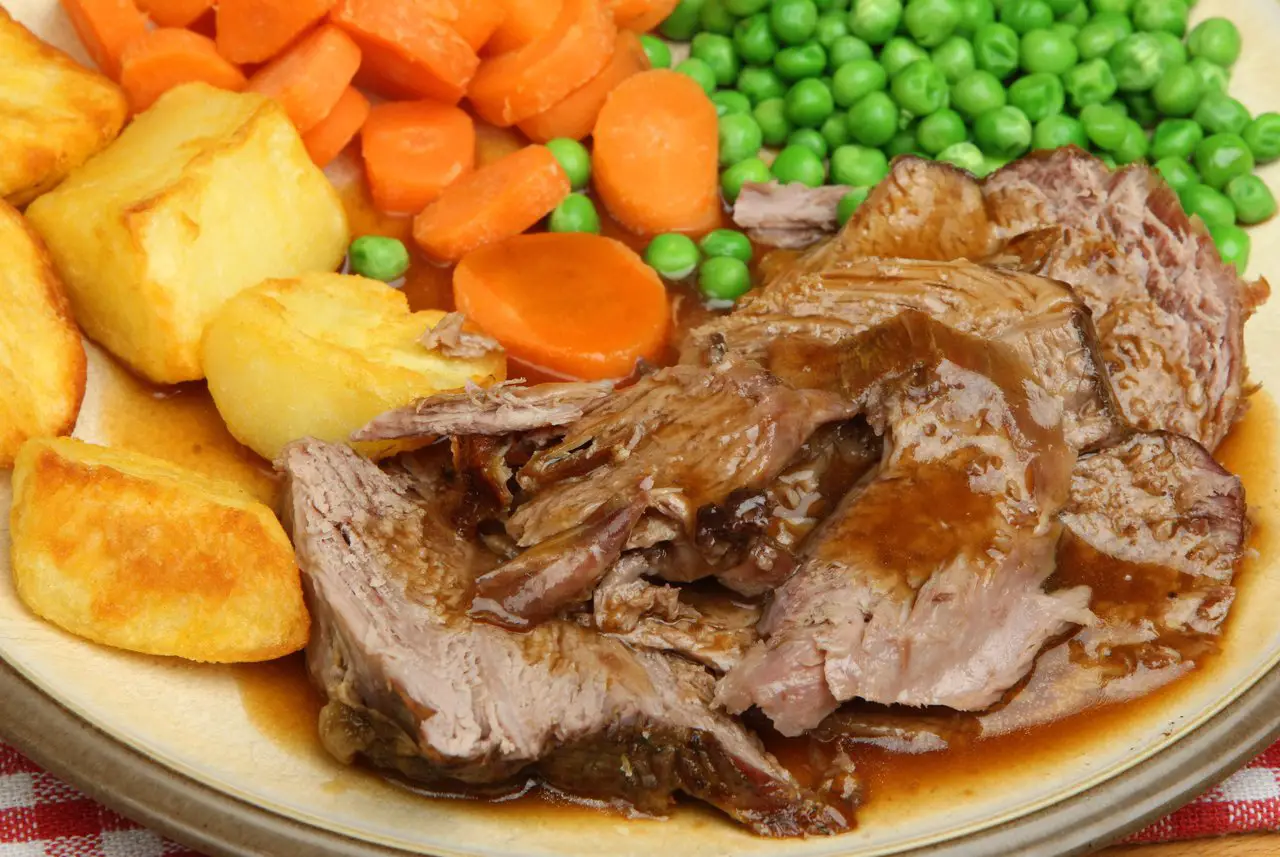 Sunday roast with all of the trimmings on a plate - roast potatoes, carrots and peas, with gravy