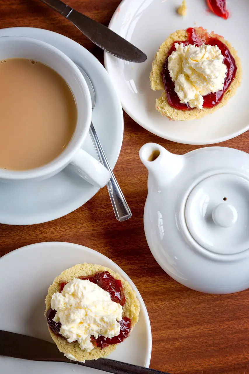 Aerial view of a cup of tea and two scones with cream and jam