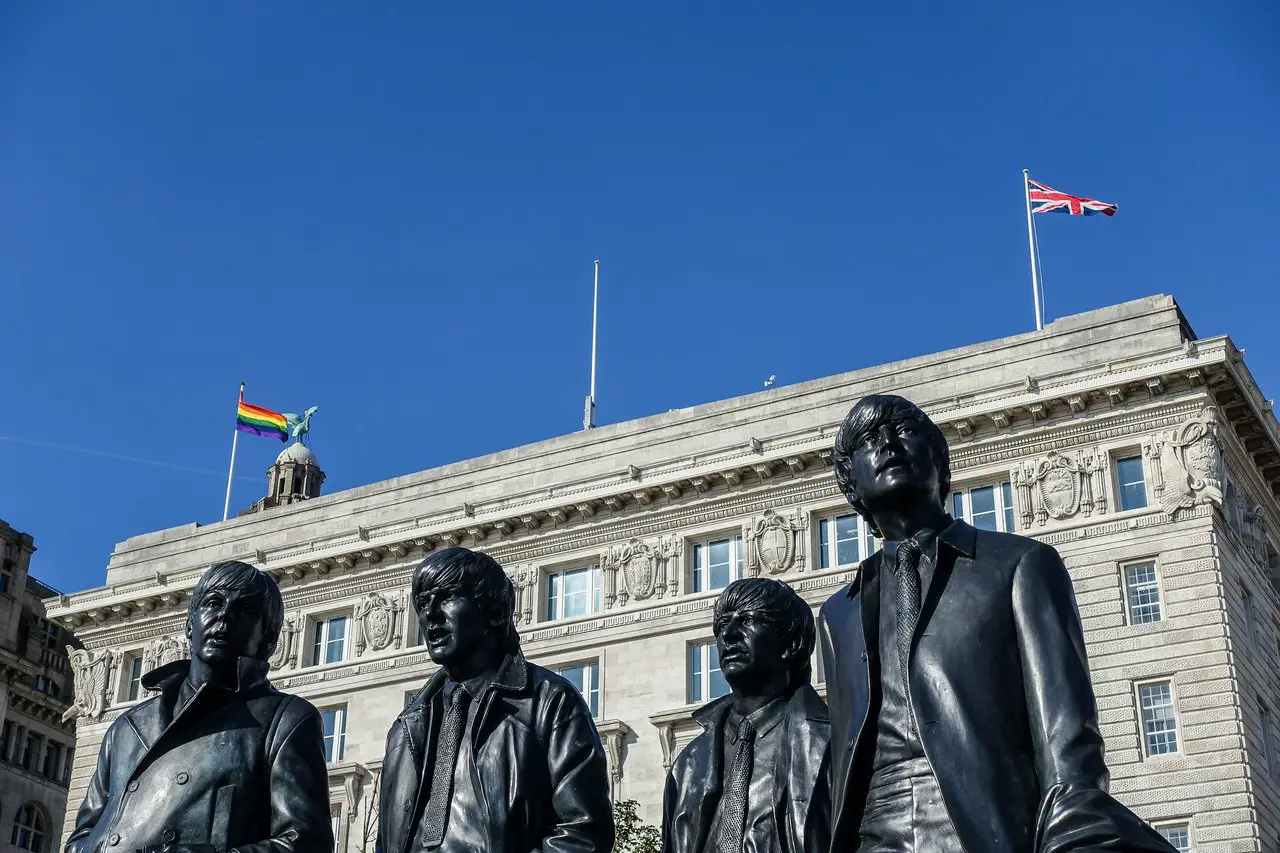 Close-up of Beatles faces at Liverpool Beatles Statue. A regal building behind is flying the Union Jack and Pride flags in the clear blue sky