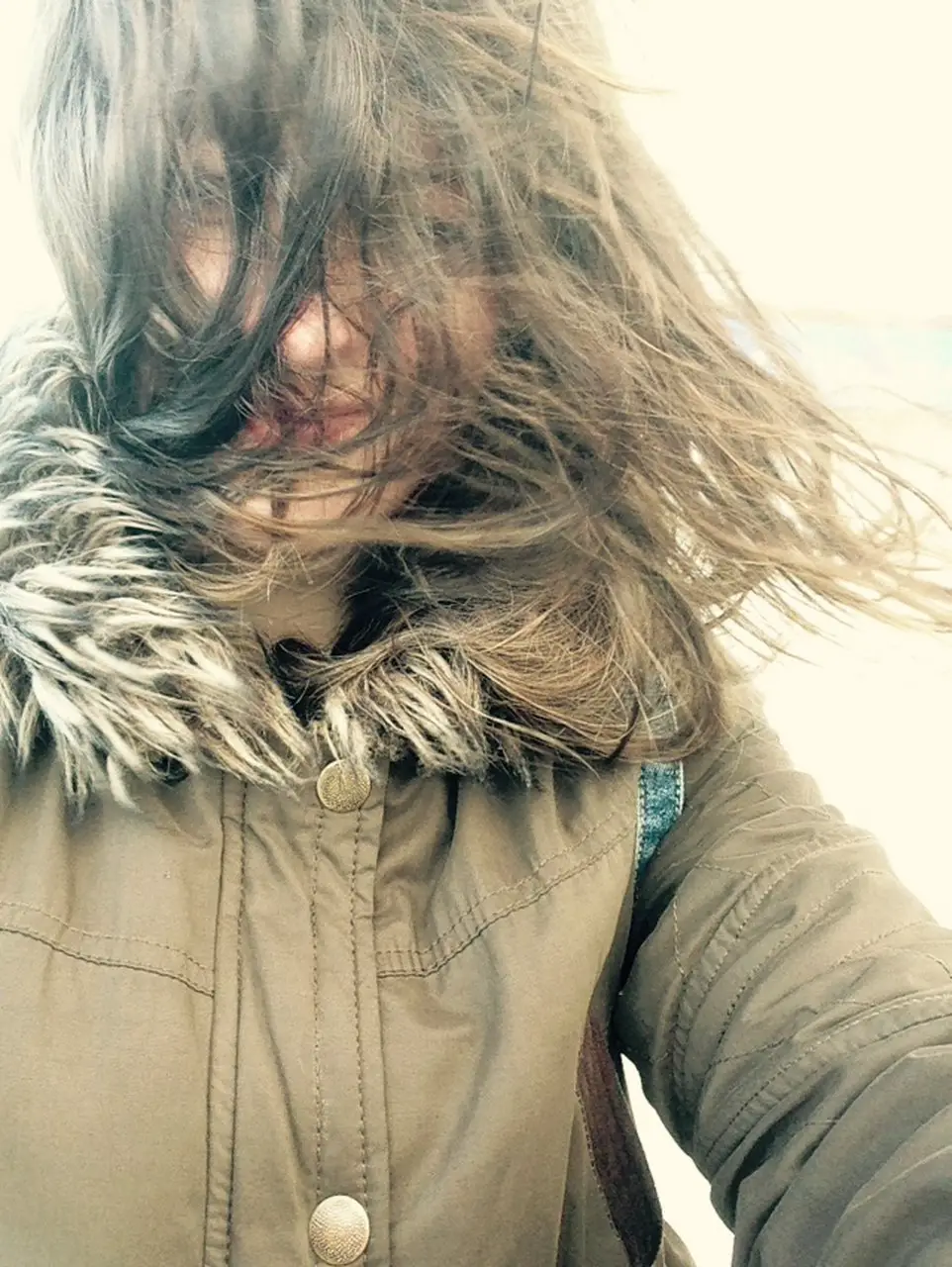 Ella, in a big coat, attempting to take a selfie on a Mersey River cruise in winter. Her hair is covering her entire face because the wind was so strong