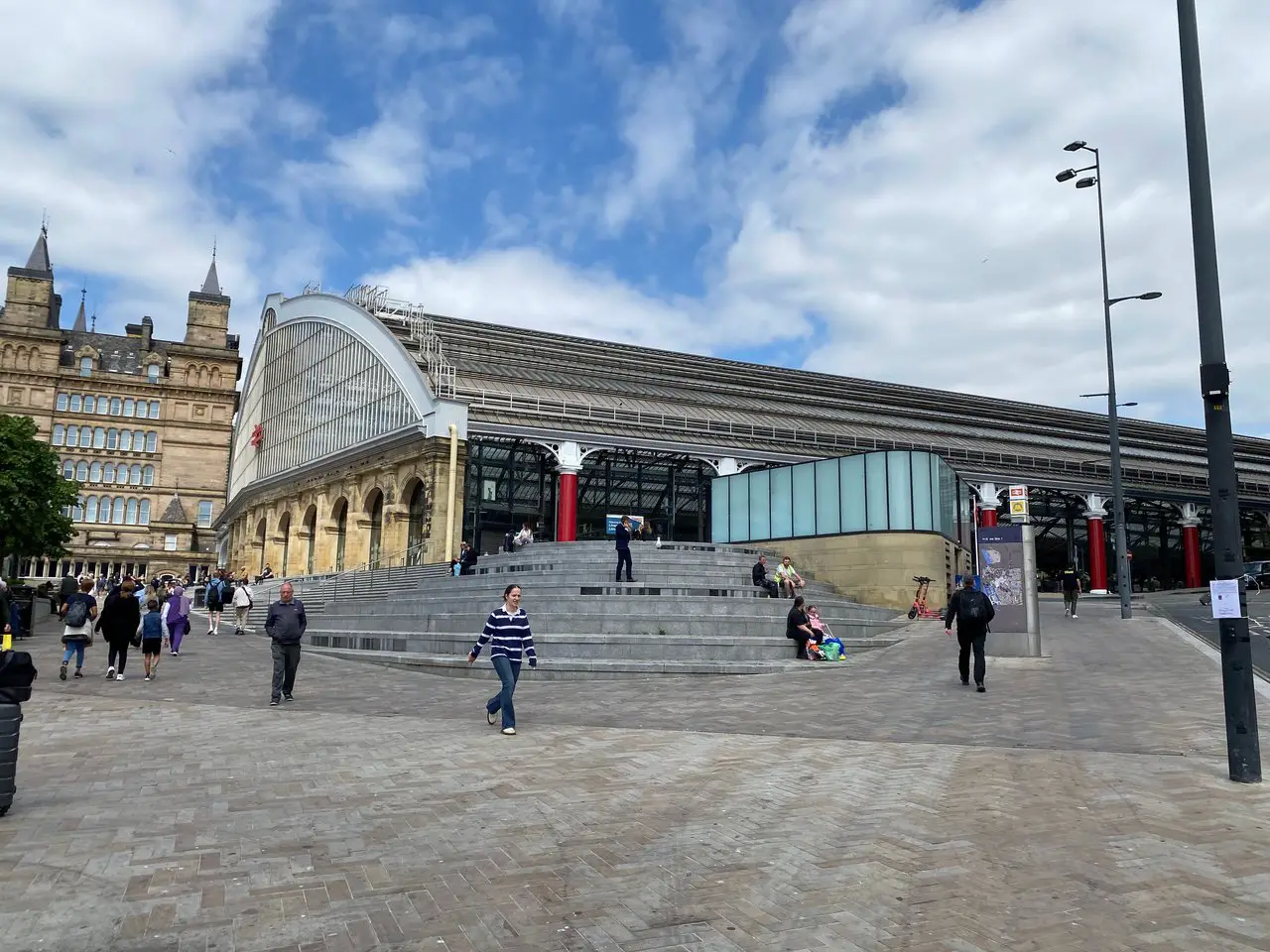 Exterior of Liverpool Lime Street station during the daytime. People are walking up and down the steps leading to the station.