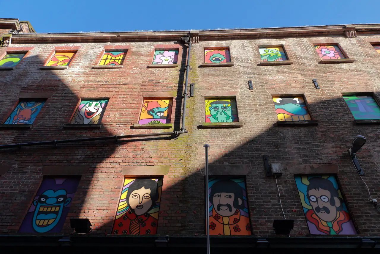 Old disused brick building in Liverpool with psychedelic Beatles murals covering the former windows. You can see this by joining one of the many Liverpool Beatles walking tours