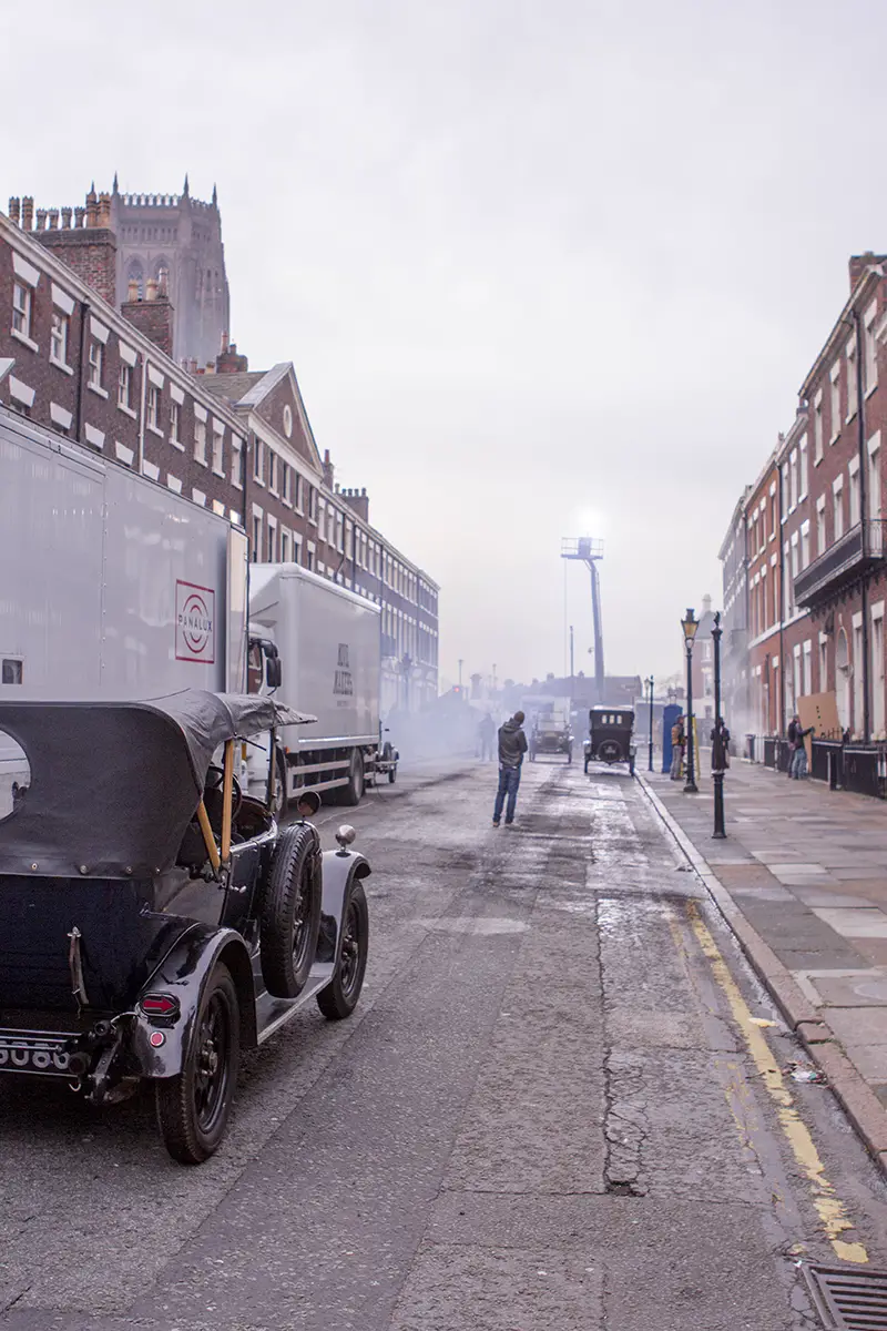 Old fashioned black car driving down a terraced street in Liverpool as part of the Peaky Blinders filming set