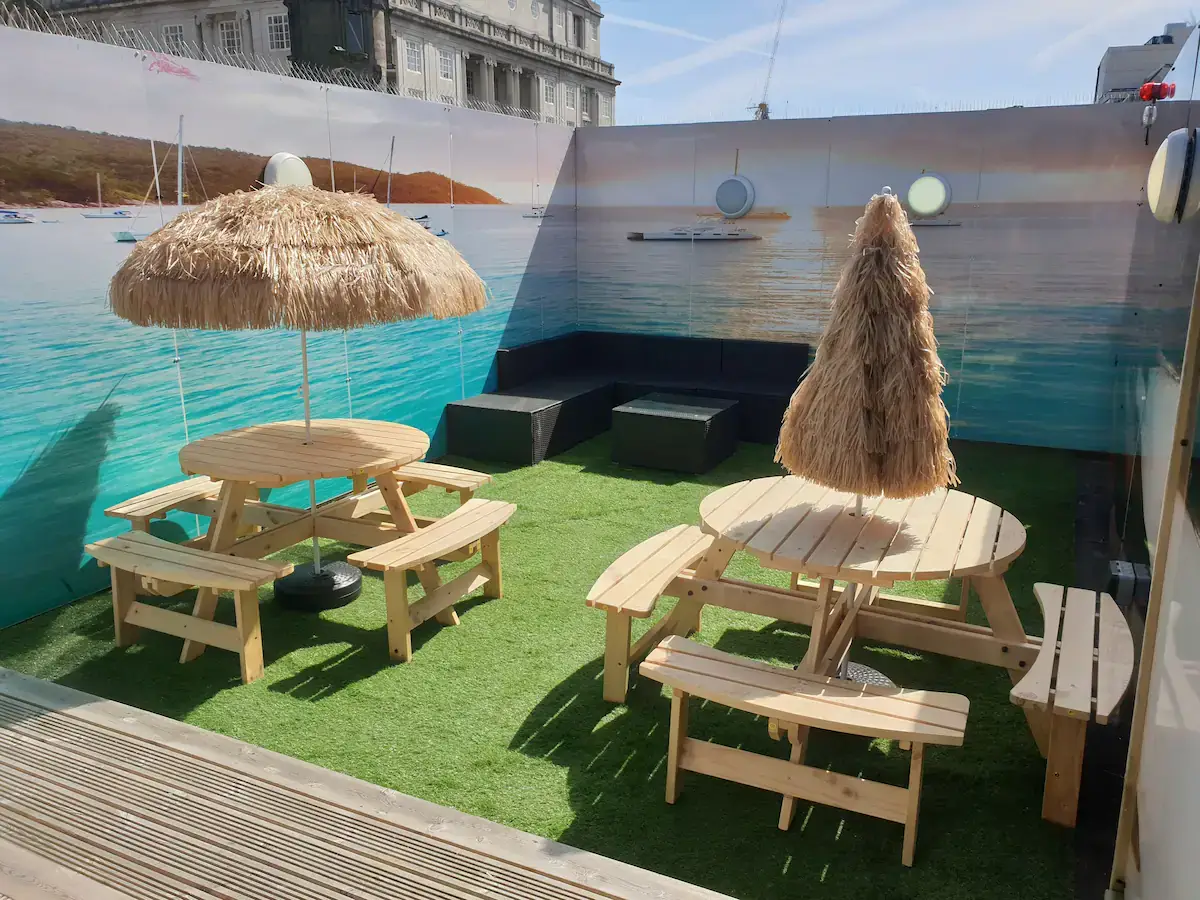 Outdoor bar showing round wooden tables with parasols. This is one of the top Liverpool city centre party apartments.