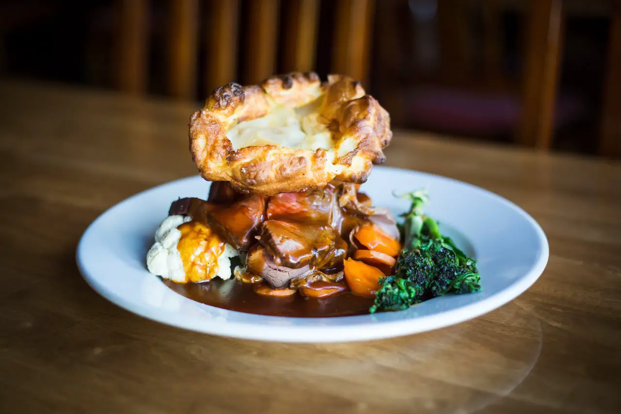 A roast dinner on a plate with a large yorkshire pudding placed on top of the food. The yorkshire pudding is an essential component to a Liverpool sunday lunch