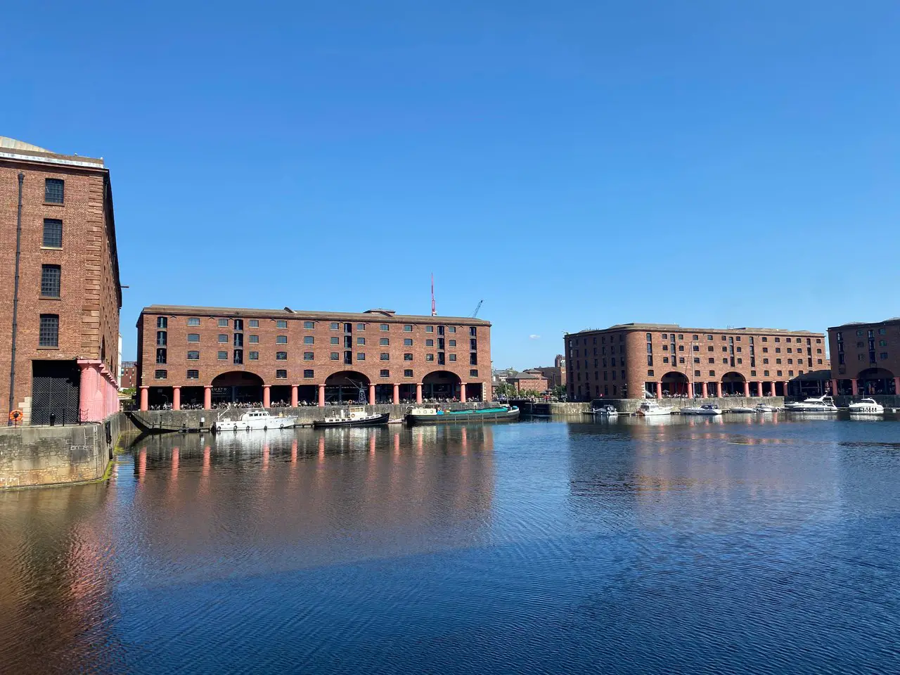 The redbrick buildings of the Albert Dock behind the water of the dock on a sunny day