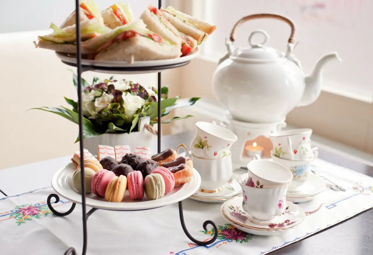 Big post of tea, stack of cute and dainty teacups, and a three-tiered afternoon tea with sandwiches, scones and macarons