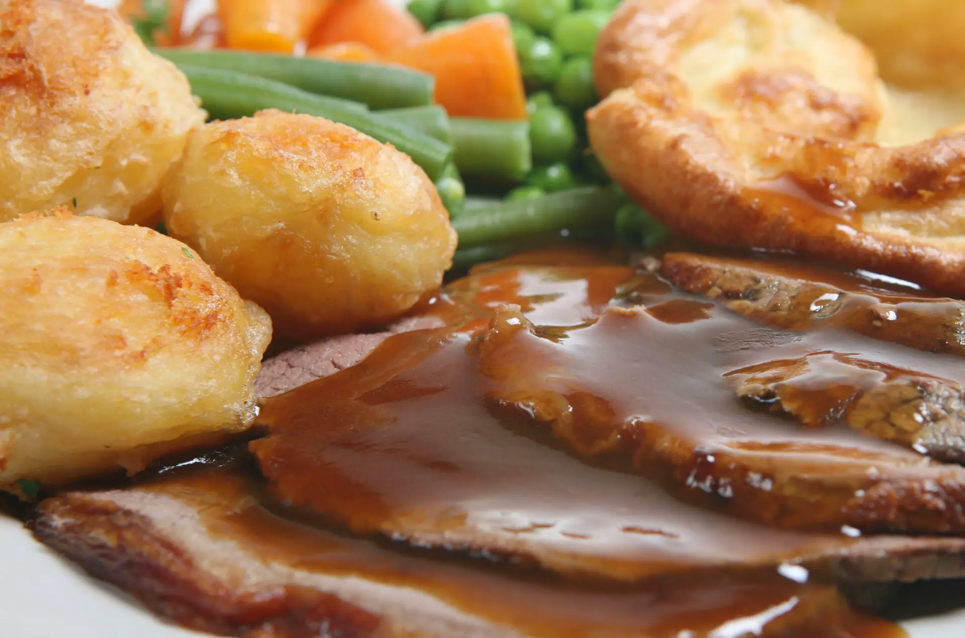 Close-up of a traditional Sunday roast dinner with beef, roast potatoes and vegetables drenched in gravy