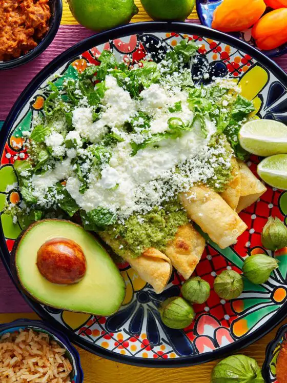 Plate of enchiladas with lime wedges and half an avocado on a plate.