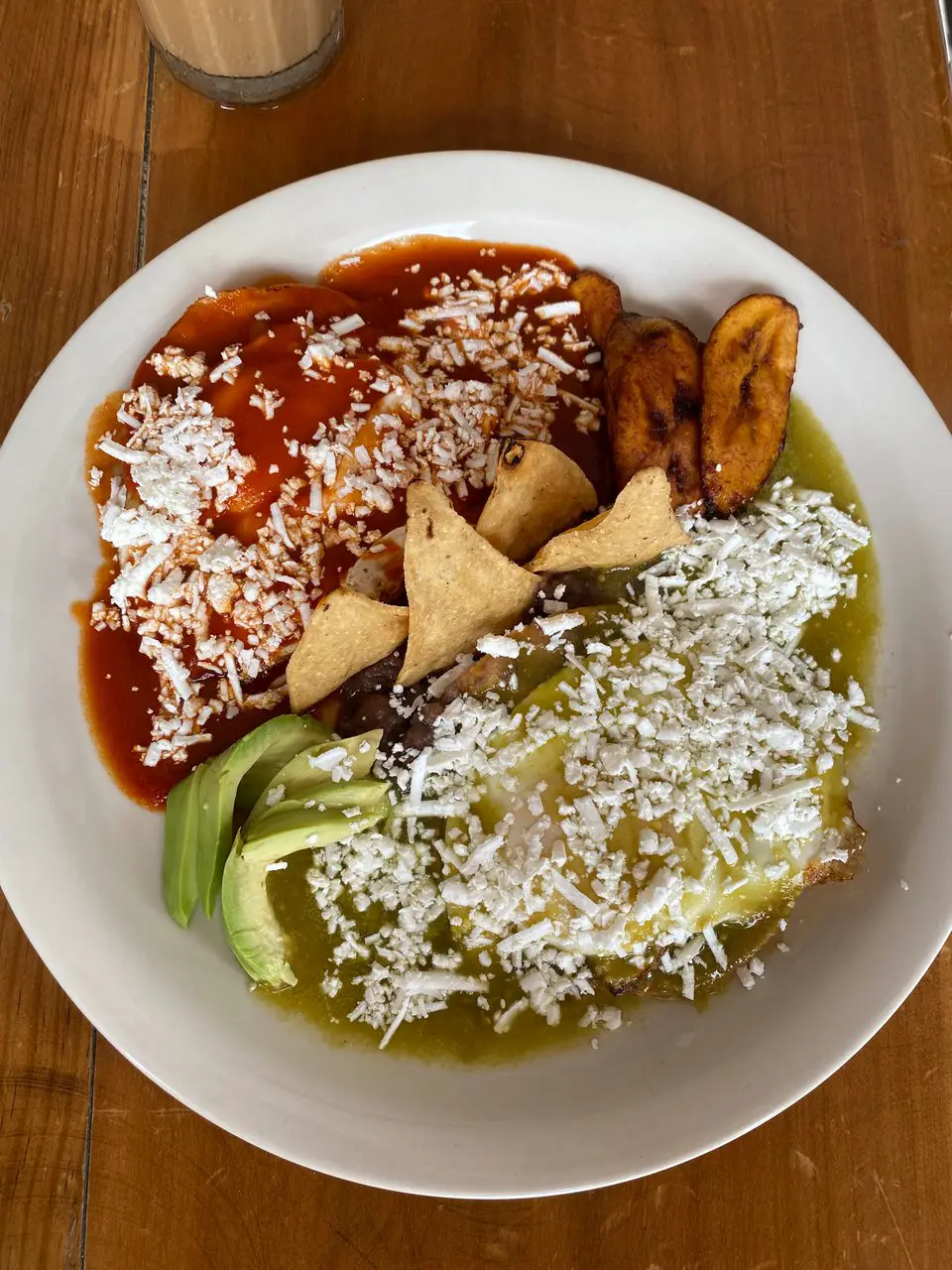 Half red and half green enchiladas on a plate, separated by a line of tortilla chips, avocado and plantain. This is typical Mexican food.