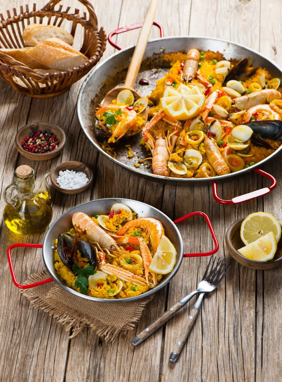 Large plate and smaller plate of Spanish paella with shrimps and mussels on top.